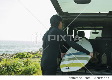 A man loading a surfboard into a car 87093363