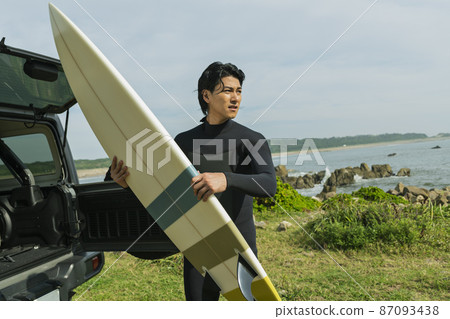 A man loading a surfboard into a car 87093438