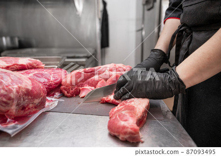 Close up of raw meat and woman butcher cutting meat with knife. 87093495