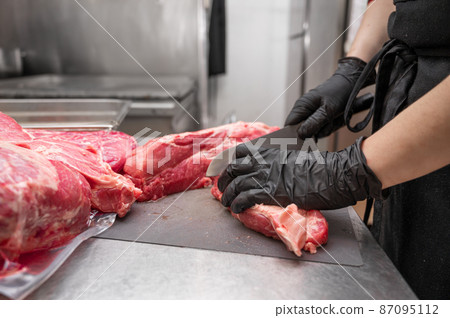 Close up of raw meat and woman butcher cutting meat with knife. Close up of raw meat and woman butcher cutting meat with knife. 87095112