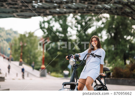 Young beautiful woman and an electric scooter, ecological transport Young beautiful woman and an electric scooter, ecological transport 87095662