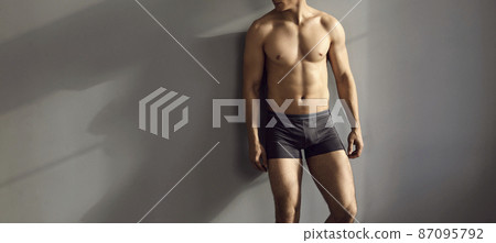 Narrow banner shot of sexy young toned man in underwear isolated on grey studio background advertise briefs. Muscular male model in underclothing garment demonstrate good body shape. 87095792