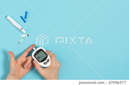Woman hands using glucometer on finger to check blood sugar level. Woman hands using glucometer on finger to check blood sugar level. 87096477