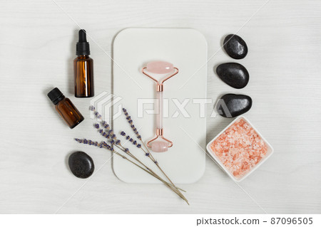 Pink quarts face massage jade roller with cosmetic products on white wooden table top view. Pink quarts face massage jade roller with cosmetic products on white wooden table top view. 87096505
