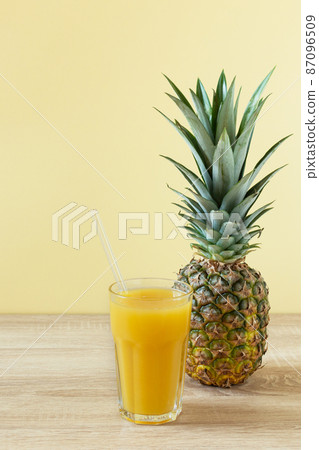 Pineapple fresh juice in glass on  wooden table over yellow background. 87096509