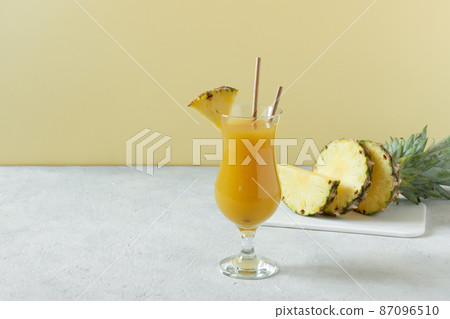 Pineapple fresh juice in glass on grey concrete table over yellow background. 87096510
