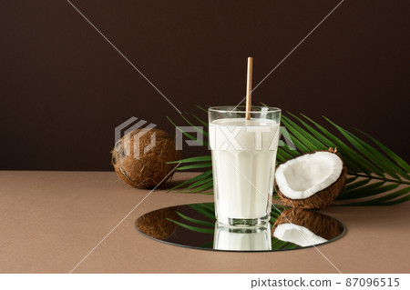 A glass of coconut vegan milk with halves of nuts over brown background. 87096515