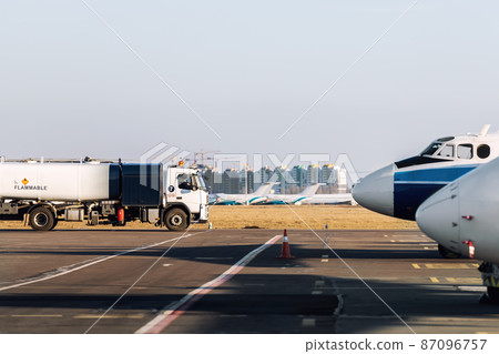 Side view small modern fuel tanker truck driving on airfield taxiway for aircraft refueling. Cistern lorry aviation gasoline. Plane gas supply. Airport maintenance handling service vehicle equipment 87096757