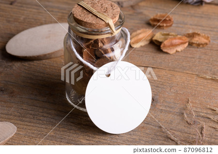 Round white tag mockup on glass jar with dry perfume a wooden background with boho decoration, element for packing 87096812