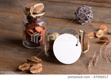 Round white tag mockup on glass jar with dry perfume a wooden background with boho decoration, element for packing Round white tag mockup on glass jar with dry perfume a wooden background with boho decoration, element for packing 87096817