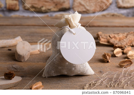 Round white gift tag mockup on gift packet on rustic wooden background with boho decoration. Round white gift tag mockup on gift packet on rustic wooden background with boho decoration. 87096841