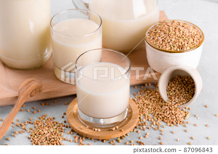 Vegan non diary buckwheat milk in glasses with buckwheat groats in a bowl on white stone table, close up 87096843