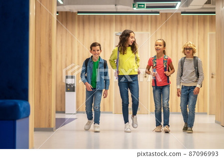 Happy schoolchildren walking chatting in corridor Happy schoolchildren walking chatting in corridor 87096993