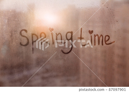 Foggy glass on window with written finger word spring time on muddy blue glass wet orange window in city on sunset Foggy glass on window with written finger word spring time on muddy blue glass wet orange window in city on sunset 87097901