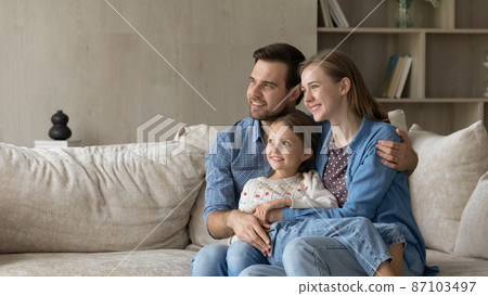 Dreamy parents and sweet daughter girl sitting on couch 87103497