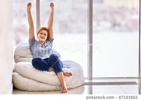 Housewarming in unfurnished apartment by young woman who sits on chair. 87103802