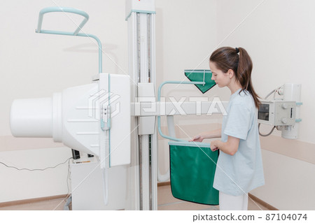 Hospital Radiology Room. Xray machine for fluorography. Woman patient scanning chest, heart or lungs in clinic office. Adult female undergoes healthcare exam. Medical X-ray equipment for radiography. Hospital Radiology Room. Xray machine for fluorography. Woman patient scanning chest, heart or lungs in clinic office. Adult female undergoes healthcare exam. Medical X-ray equipment for radiography. 87104074