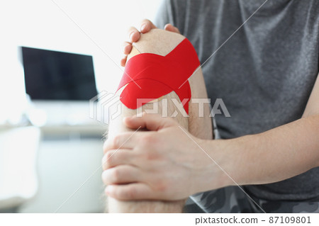 Man sit in hospital with kinesiology tape on knee, pain in leg, rehabilitation after injury 87109801