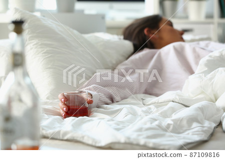 Woman in bed after fun night, hold glass with alcoholic drink, drunk female sleep Woman in bed after fun night, hold glass with alcoholic drink, drunk female sleep 87109816