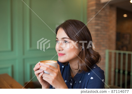 Portrait of happy young business woman with mug in hands drinking coffee in the morning at restaurant 87114077