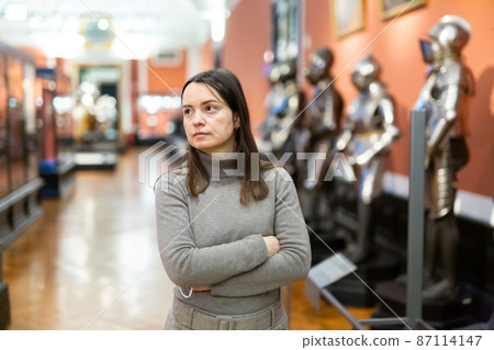 Female museum visitor examining with interest ancient armor 87114147