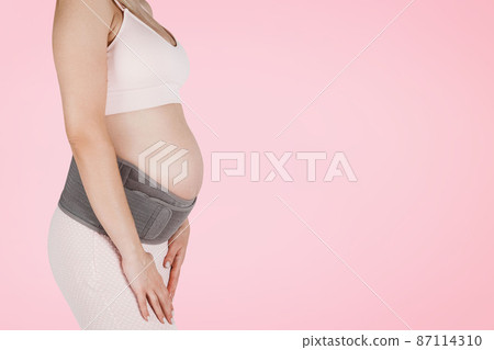 Pregnant woman belly in prenatal pregnancy maternity belt isolated on pink background. Orthopedic abdominal support waist, back, abdomen band. Belly Brace for pregnancy. Horizontal banner or poster. 87114310