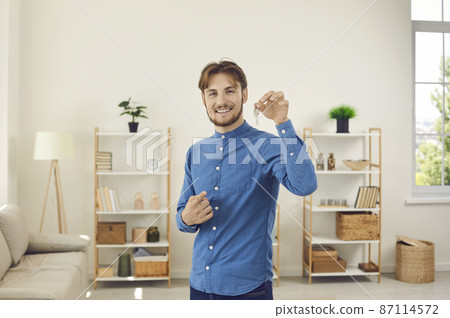 Happy and successful Caucasian man excited by moving into new apartment. Young man who is first buyer, homeowner or tenant of apartment shows keys while looking at camera. Mortgage concept. Happy and successful Caucasian man excited by moving into new apartment. Young man who is first buyer, homeowner or tenant of apartment shows keys while looking at camera. Mortgage concept. 87114572