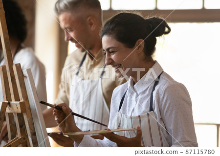 Joyful laughing young Indian woman drawing on easel. 87115780