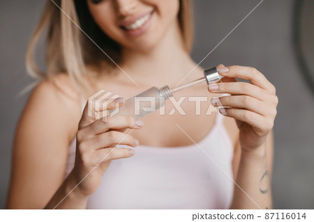 Moisturizing with serum, collagen and hyaluronic acid. Woman with glowing skin holding bottle of essential oil, closeup Moisturizing with serum, collagen and hyaluronic acid. Woman with glowing skin holding bottle of essential oil, closeup 87116014