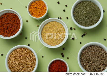 Set of different spices in bowls on green background Set of different spices in bowls on green background 87116485