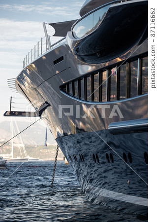 The mesmerizing reflection of the water on the glossy side of a huge yacht anchored, chrome details, chains and ropes to the muring descend into the water The mesmerizing reflection of the water on the glossy side of a huge yacht anchored, chrome details, chains and ropes to the muring descend into the water 87116662
