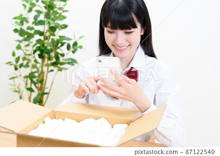 將裝有緩衝材料的紙板箱放入並操作智能手機的高中女生 送貨上門 郵購 跳蚤市場應用程序拍賣 87122540