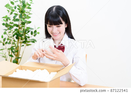 High school girls who put in cardboard luggage with cushioning material and operate smartphones Home delivery delivery mail order flea market app auction 87122541