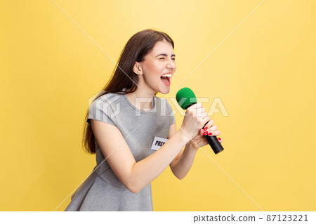 Emotional young girl, female reporter holding reporter microphone isolated on yellow studio background. Concept of social media, press, news, information Emotional young girl, female reporter holding reporter microphone isolated on yellow studio background. Concept of social media, press, news, information 87123221