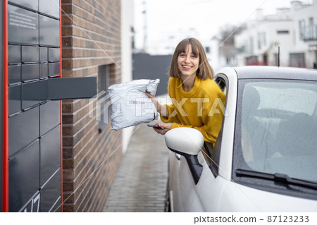 Woman getting parcel from the post office terminal right out of the car window on the go 87123233