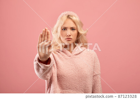 Young serious woman making the hand stop sign against pink background. Stop abuse, discrimination, violence concept 87123328