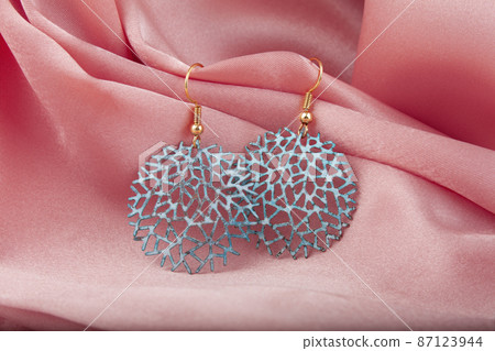 Metal earrings on pink silk background. close up shot Metal earrings on pink silk background. close up shot 87123944