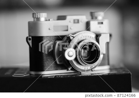 Black and white vintage old photography film camera with lens on a book. Close up shot Black and white vintage old photography film camera with lens on a book. Close up shot 87124166