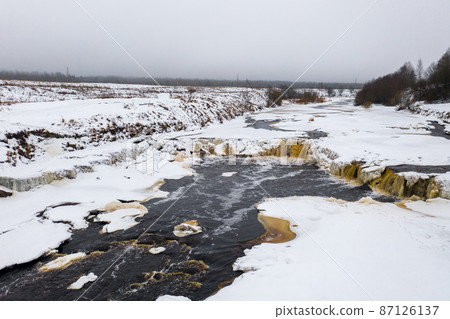Winter aerial view of the river valley and waterfall. Freezing river. The ice and the banks are covered with snow. Winter aerial view of the river valley and waterfall. Freezing river. The ice and the banks are covered with snow. 87126137