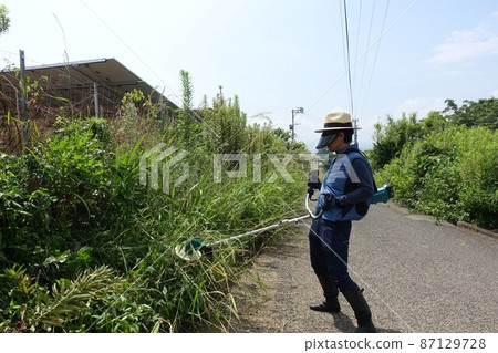 Weeding work along the road, a man mowing grass 87129728