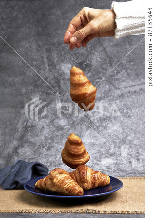 Hand of woman dropping croissants on a plate. Healthy breakfast Hand of woman dropping croissants on a plate. Healthy breakfast 87135643