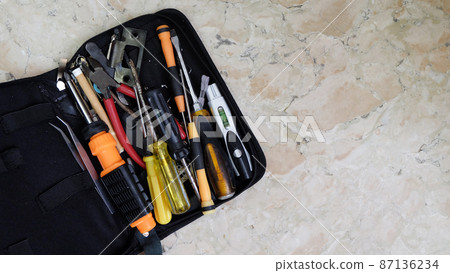 A tool bag with unsorted tools of tweezers, screwdrivers, pliers, and others. Placed on a marble surface with copy space on the right. A tool bag with unsorted tools of tweezers, screwdrivers, pliers, and others. Placed on a marble surface with copy space on the right. 87136234
