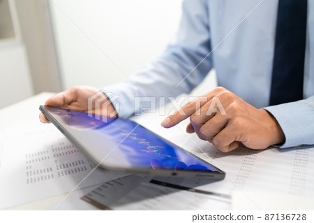 Working Man Conept The male employee sitting at his desk, holding a tablet, and touching the screen of his work Working Man Conept The male employee sitting at his desk, holding a tablet, and touching the screen of his work 87136728