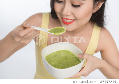 Portrait of asian woman eating/holding a plate of green vegetables soup 87137215