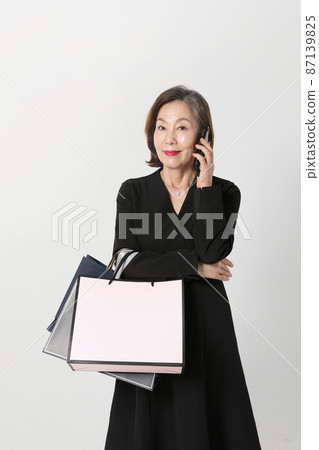 fashionable Asian Korean senior woman, holding a shopping bag, calling on phone 87139825