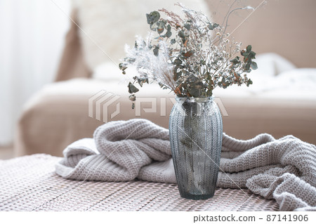 Home composition with a glass vase with dried flowers on a blurred background. 87141906