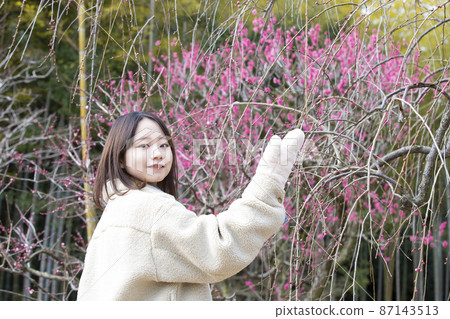 在大阪府吹田市的 70 年世博會紀念公園，梅花初開的背景下，一位微笑的年輕女子。 87143513