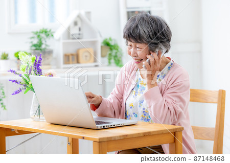 Senior woman touching a computer while making a phone call with a smartphone 87148468