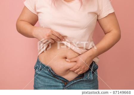 Woman hand holding excessive belly fat, overweight concept. Overweight female wearing a jeans 87149668