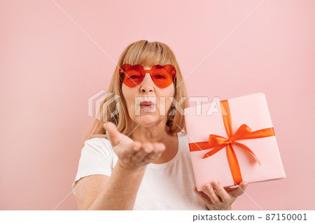 Portrait of happy and positive caucasian 40s 50s woman gives an air kiss over bright pink color background Portrait of happy and positive caucasian 40s 50s woman gives an air kiss over bright pink color background 87150001